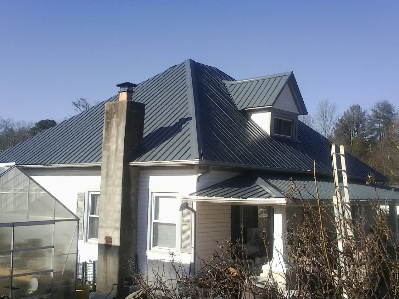 Dark blue standing seam metal roof on a white farmhouse with dormer — Slate & Tile Roof Repair by Roofing Brothers in Humble