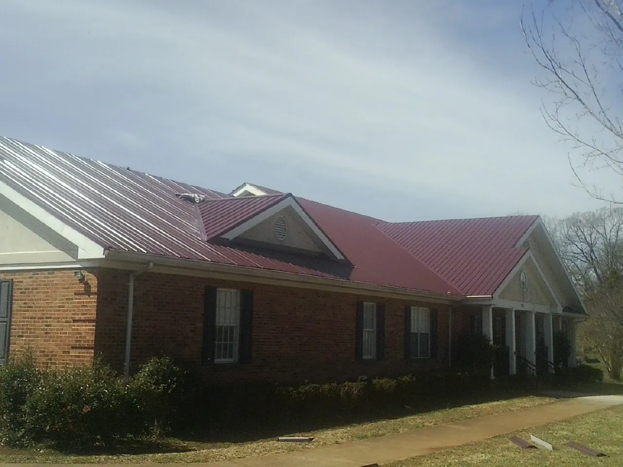 Red metal roof with gabled entries on a long brick building, from a Hail Damage Roof Repair job in Humble