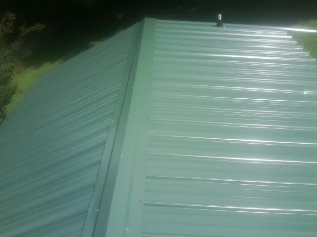 New green metal panels meeting at the ridge of a roof — Flat Roof Repair work by our crew in Humble