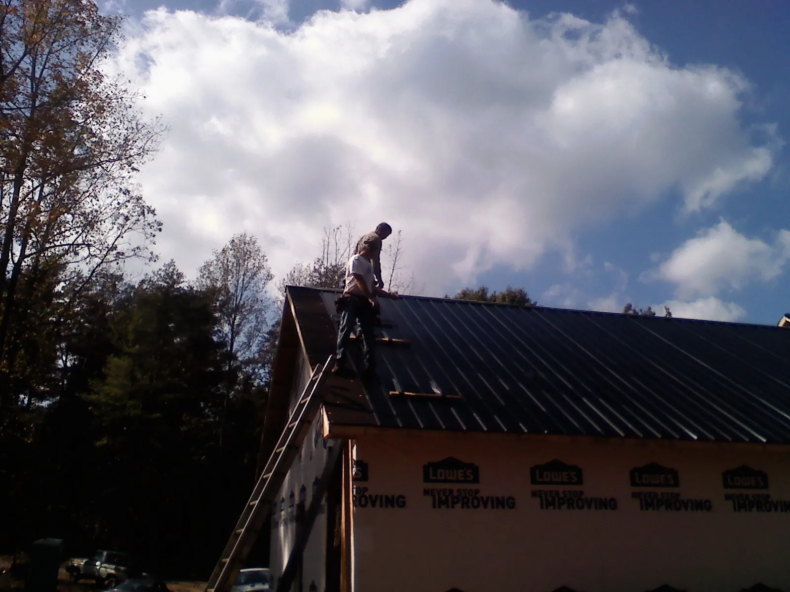 Roofer fastening dark metal panels high against a cloudy sky, from a Roof Inspection job in Humble