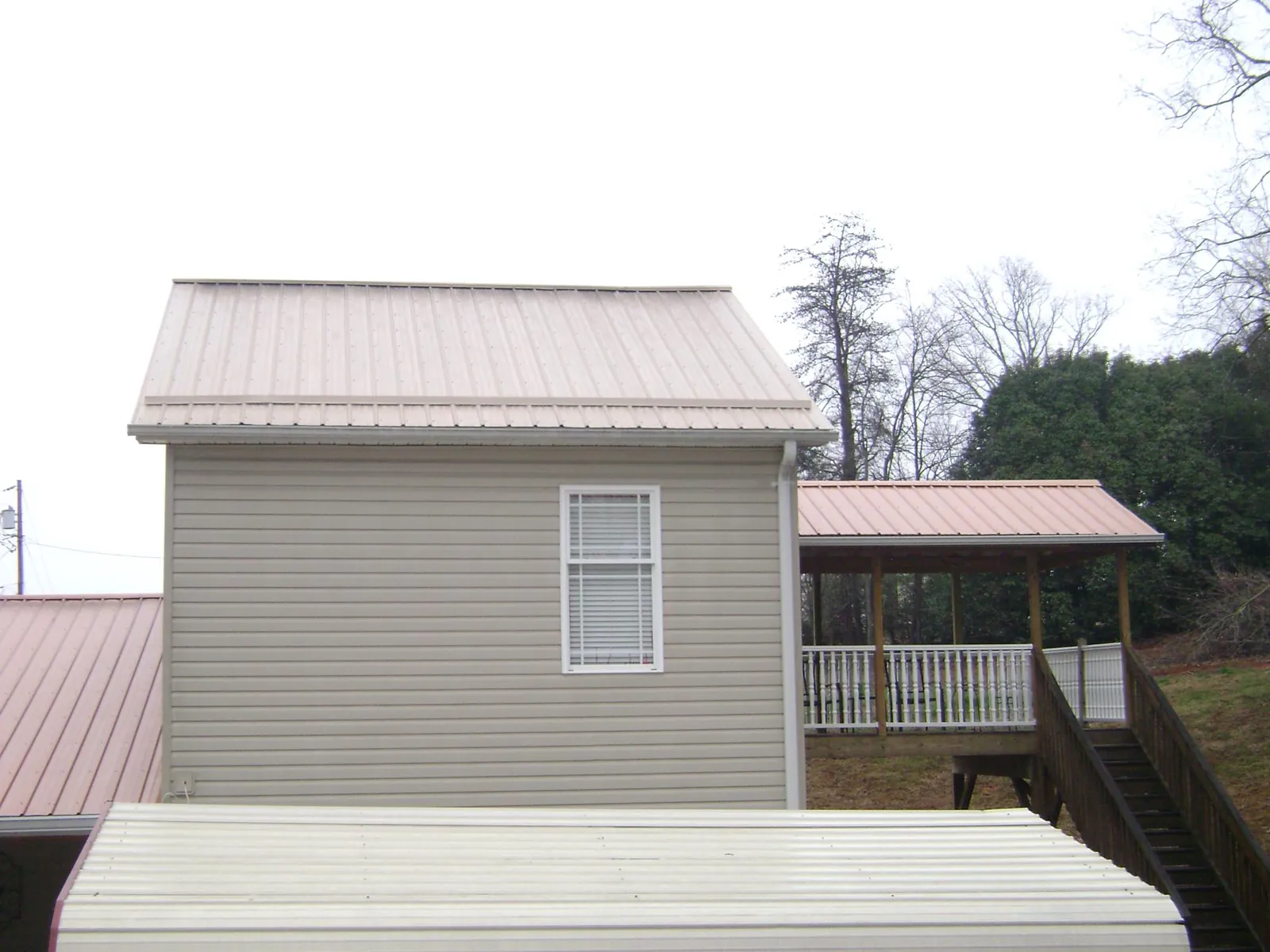 Tan metal roofs on a two story addition and attached porch, from a Roof Replacement job in Humble